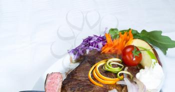 fresh juicy beef ribeye steak grilled with lemon and orange peel on top and vegetables beside with sour cream