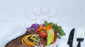fresh juicy beef ribeye steak grilled with lemon and orange peel on top and vegetables beside