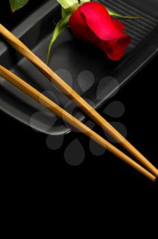 red rose on a japanese black plate with chopsticks over black