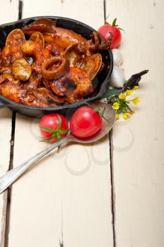 fresh seafood stew prepared on an iron skillet ove white rustic wood table 