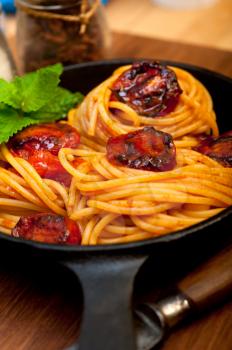 italian spaghetti pasta and tomato with mint leaves on iron skillet over wood board 