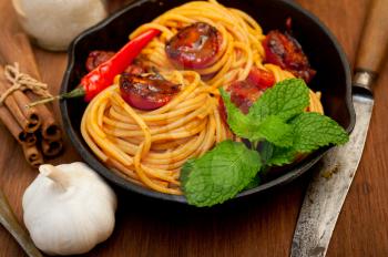 italian spaghetti pasta and tomato with mint leaves on iron skillet over wood board 