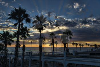 Royalty Free Photo of an Oceanside Pier with Palm Trees at Sunset