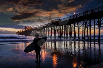 A young surfer sees nothing but flat. Oceanside Pier is silhouetted during another Southern California sunset. Oceanside is 40 miles North of San Diego, California.