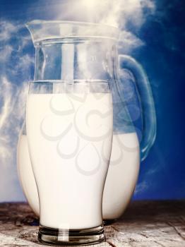 Milk jug and glass over old wooden desk with cloudy skies as background