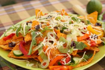 Heap of nachos with vegetables on green plate.