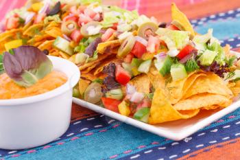 Nachos, vegetables and cheese sauce on colorful towels.