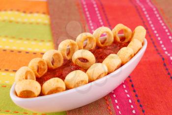 Potato rings and red sauce isolated on colorful tablecloth.