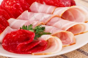 Salami and bacon on plate closeup image.