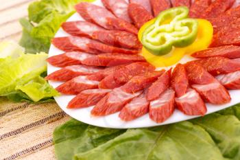 Fresh sausages, peppers in plate and green salad leaves on bamboo mat background.