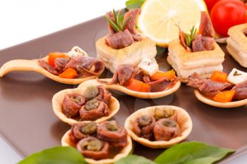 Anchovies in pastries, lemon, tomato and basil on brown plate.