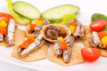 Fish and peppers on crackers with vegetables on white plate.