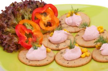 Cream on crackers and vegetables on green plate.