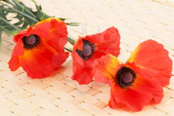Red fabric poppies on bamboo background.