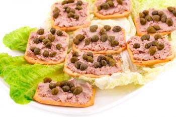 Meat pate with capers on crackers and lettuce on plate.