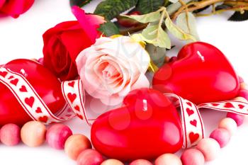 Red heart candles, wooden necklace, ribbon and roses on white background.