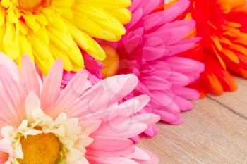 Colorful fabric daisies on wooden background, closeup picture.