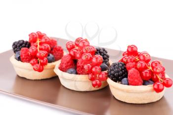 Fresh ripe berries in tartlets on brown plate.