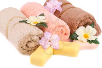 Rolled towels, soaps and flowers on white background.