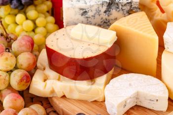 Various type of cheese and grapes on wooden board closeup picture.