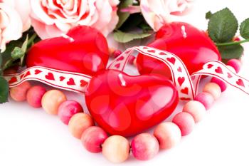 Red heart candles, wooden necklace and ribbon on white background.
