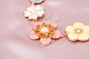 Stylish necklace with stones and pearls on pink silk background.