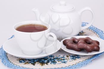 Cup of tea, kettle, chocolate cookies on blue and beige patterned napkin.
