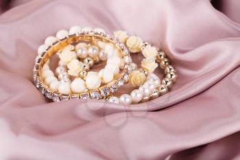 Stylish bracelets with pearls and stones on fabric background.