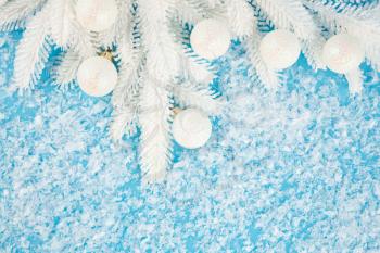 Christmas decoration with white balls and fir tree branch on the artificial snow background.