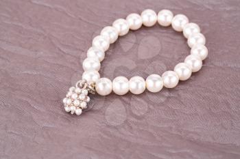 Stylish bracelet with pearls on fabric background.