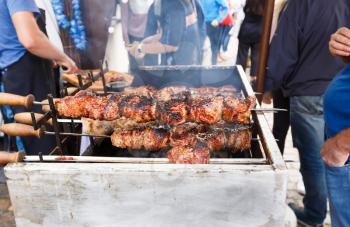 Barbecue skewers on open grill, people waiting tasty food.