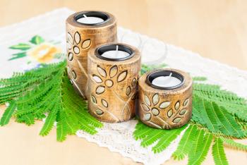 Three brown ancient style candle nests and green leaves on cloth.