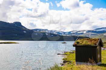 Landscape with mountains, lake, traditional old house, sky and clouds in Norway.