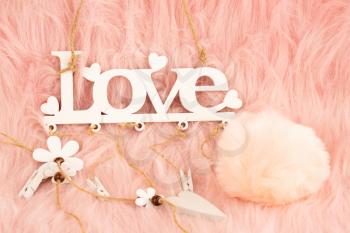 White wooden word love and fluffy ball on pink fur background.