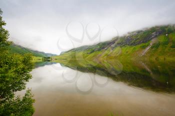 Landscape with fjord, village and mountains in Norway, foggy day.