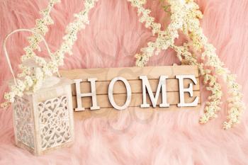 Wooden sign with word Home, lantern and white flowers on pink fur background.