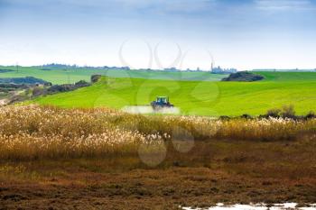 Tractor spraying the chemicals on the large green field near the swamp in Cyprus.
