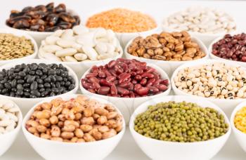 The collection of different beans in the ceramic bowls on a white background.