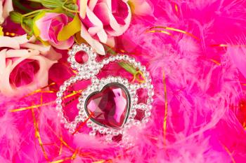 Valentine decoration with jewelry heart and roses on pink feathers background.