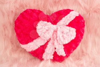 Pink heart with ribbon on fur background.