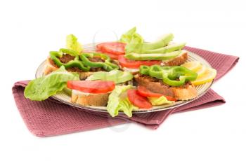 Sandwiches with cheese, sundried tomatoes, pepper, avocado and seeds, lettuce, lemon on beige  plate on towel isolated on white background.