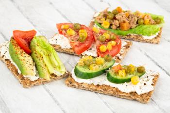 Sandwiches with crackers, cheese, tuna fish and vegetables on gray wooden background.