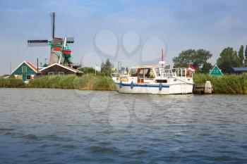 Traditional, authentic dutch windmill and boat at the river Zaam in Zaanse Schans village.