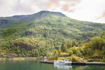 Landscape with Naeroyfjord, ship, mountains, traditional houses and dark clouds in Norway.