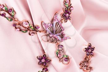 Stylish necklace and earrings on pink fabric background.
