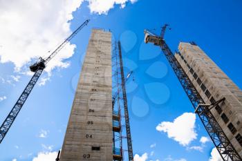 Construction site with cranes and unfinished buildings on the blue sky background.