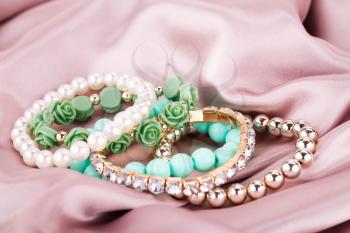 Stylish bracelets with pearls and stones on fabric background.