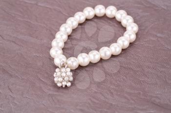 Stylish bracelet with pearls on fabric background.
