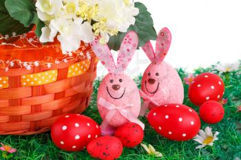 Easter decoration with bunnies, eggs and flowers in basket on artificial grass.