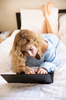 Woman in blue sweater with laptop lying in the bed.